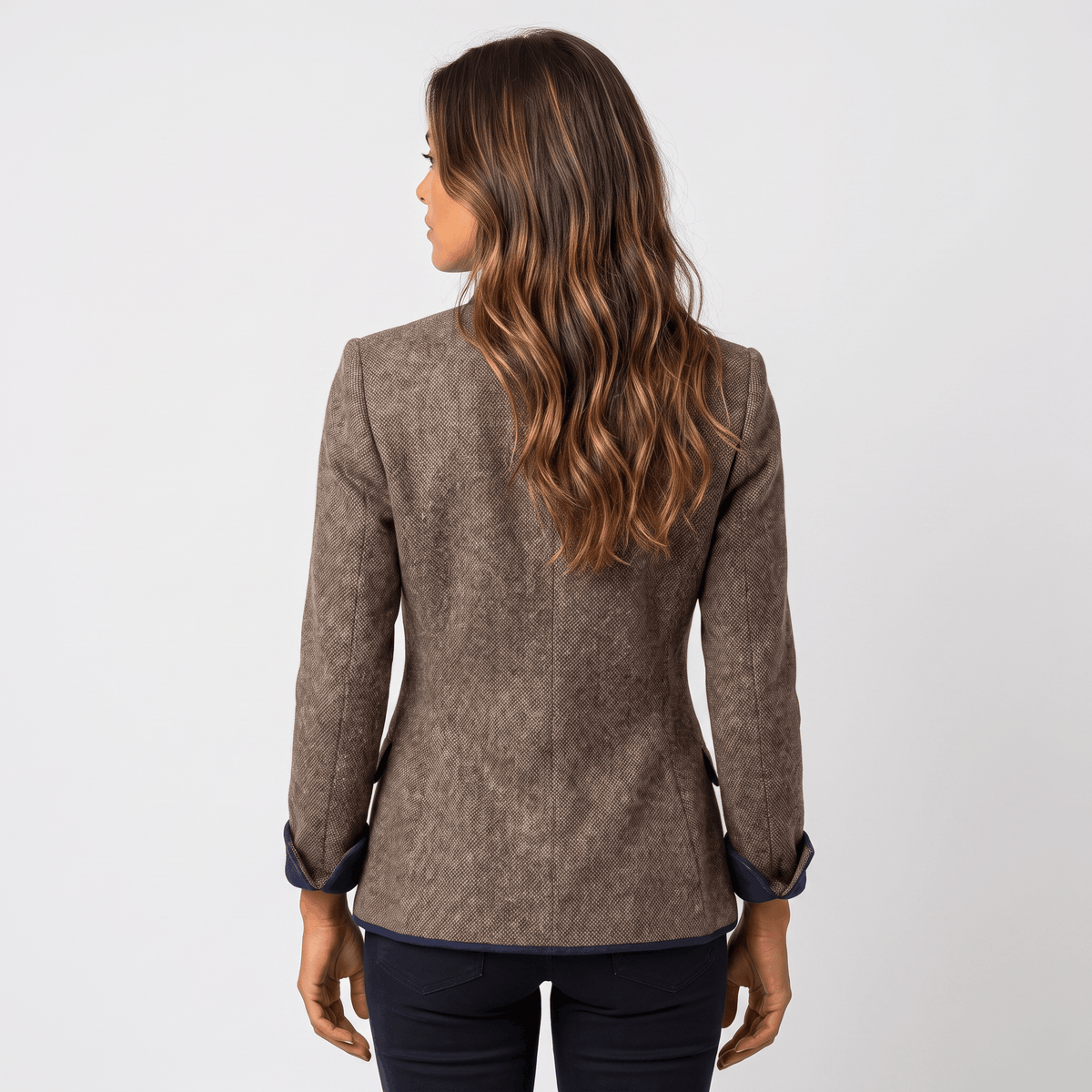 Back view of a woman wearing a brown tweed blazer with contrasting navy trim and a tailored silhouette.