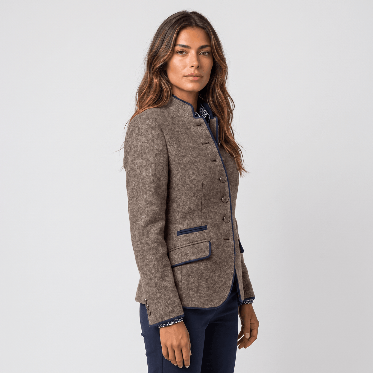 Side view of a woman wearing a brown tweed blazer with navy-trimmed lapels, button closure, and tailored fit.