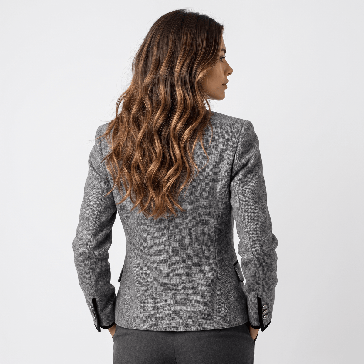 Back view of a woman wearing a gray tweed blazer with a tailored fit and contrasting dark trim.