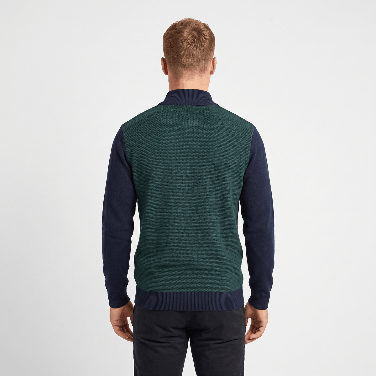 Back view of a men's green and navy color block quarter-zip knit sweater with ribbed texture and stand collar.