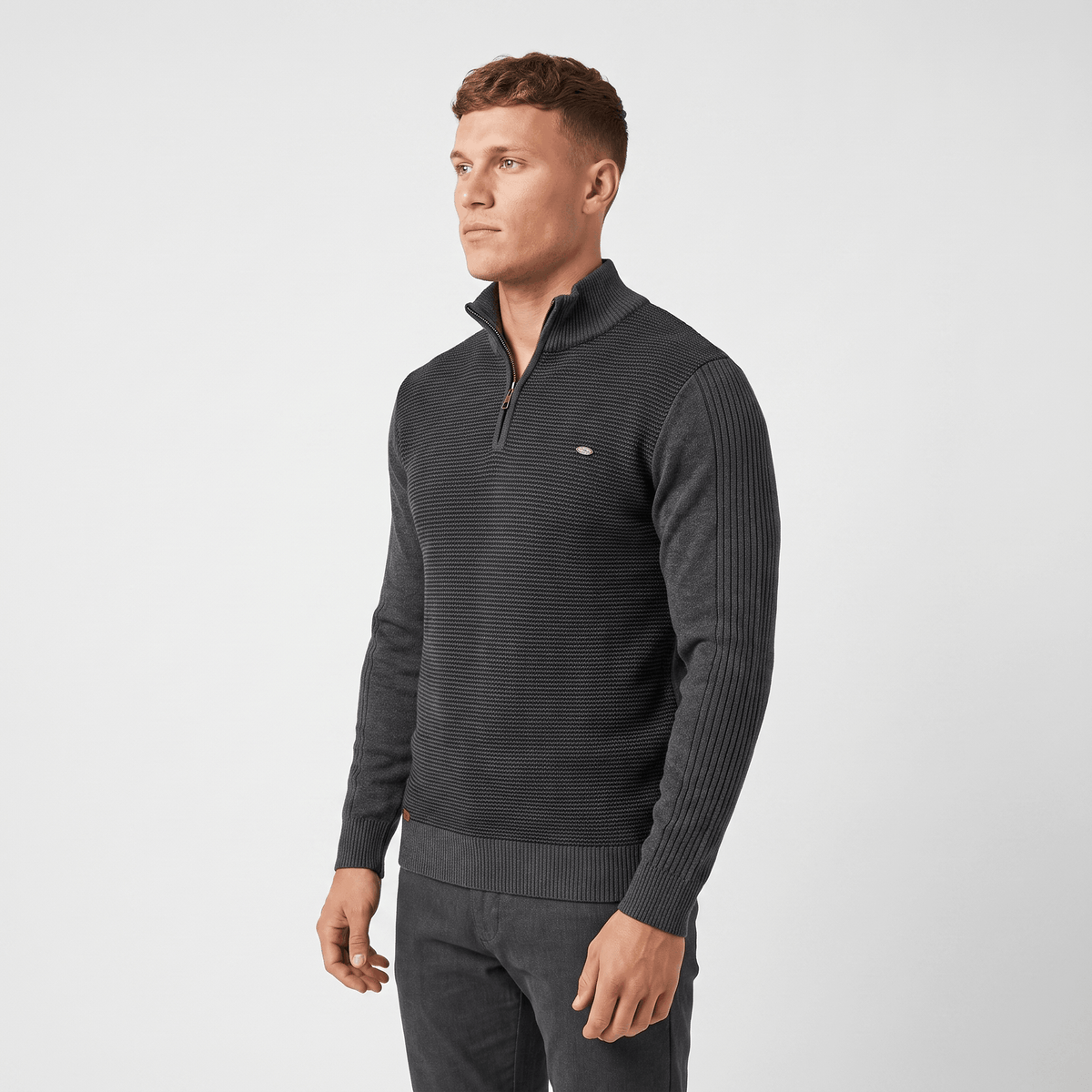 Side view of a man wearing a charcoal ribbed quarter-zip sweater with a stand collar and long sleeves.
