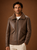 Brown shearling aviator jacket for men with shearling lining, leather shell, zip front, and flap pockets, worn by a male model