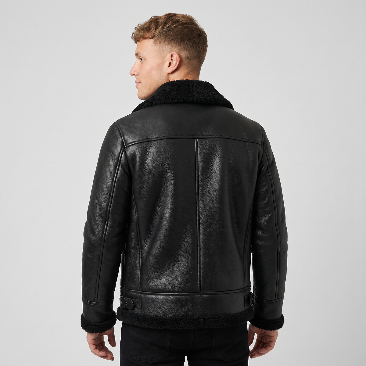 A man wearing a black shearling leather jacket with plush lining and buckle collar, shown from the back