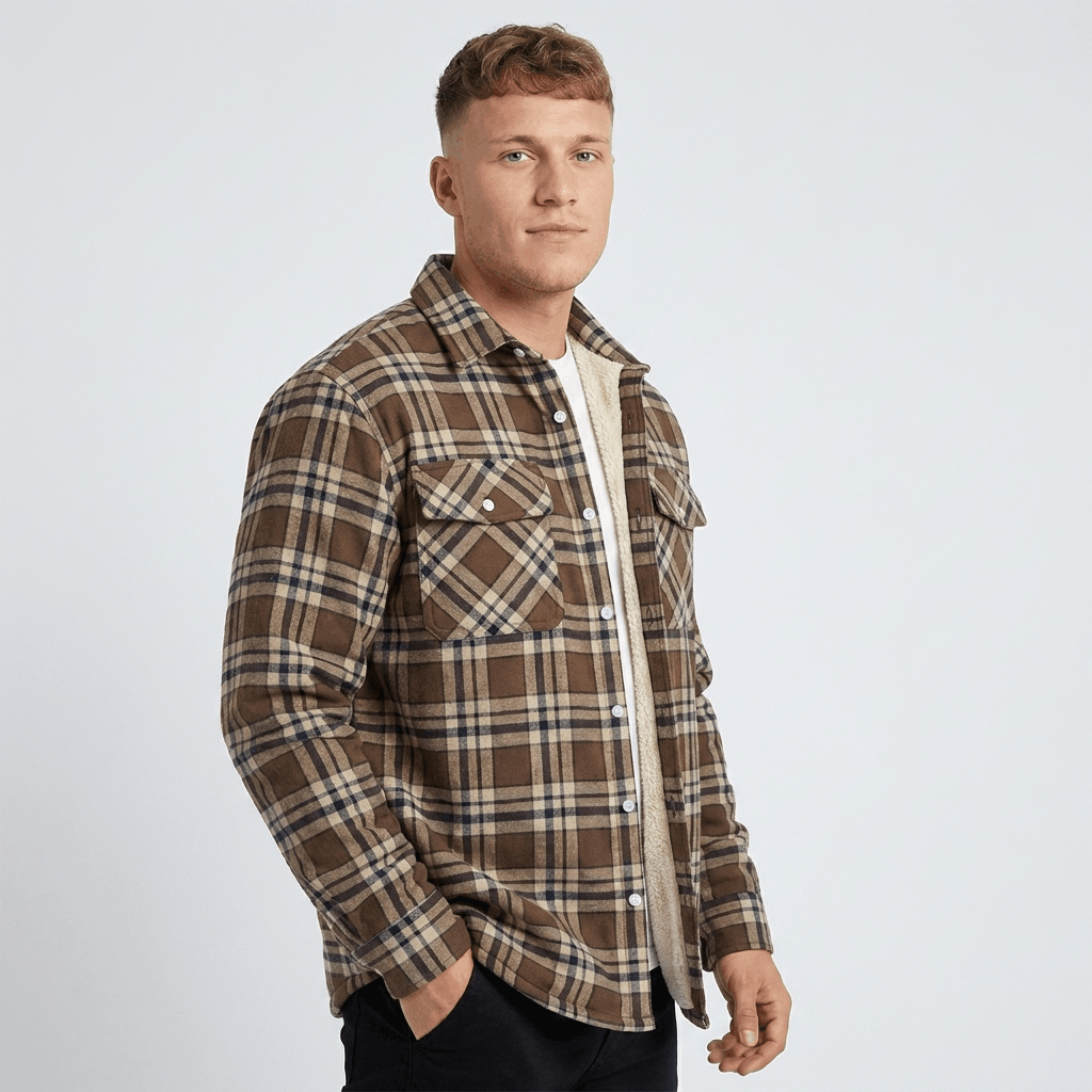 Man wearing a brown and cream plaid sherpa-lined overshirt jacket with a button-front closure, pointed collar, chest pockets, and long sleeves over a white shirt.