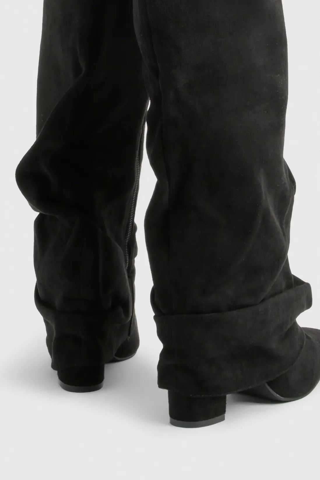 Black suede slouchy knee-high boots worn with black pants, shown from the back.