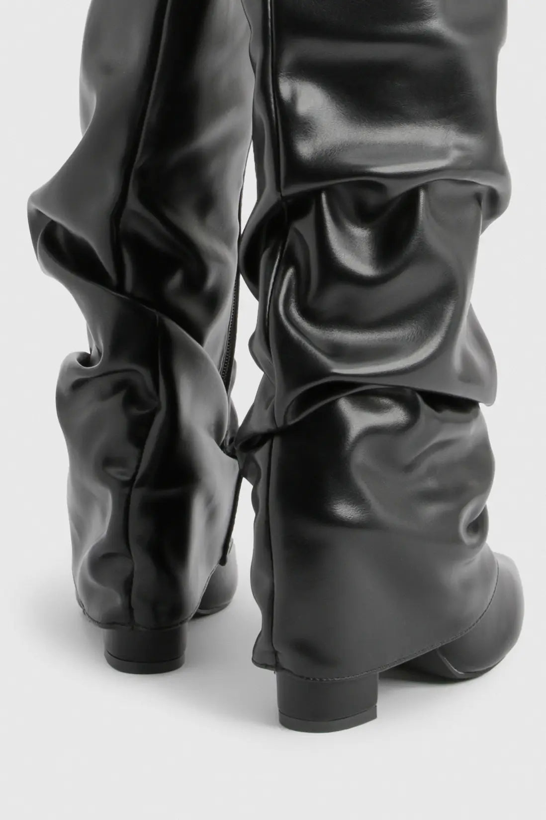 Close-up of black leather slouchy knee-high boots showing the ruched shaft and heels.