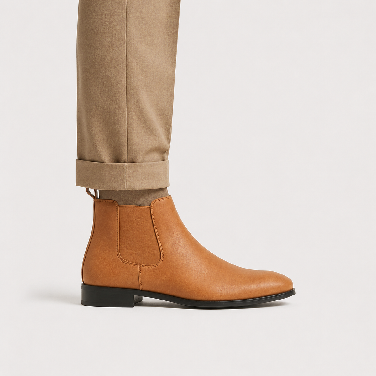 Brown leather Chelsea boots with elastic side panels, round toe, and low block heel worn with cuffed trousers.