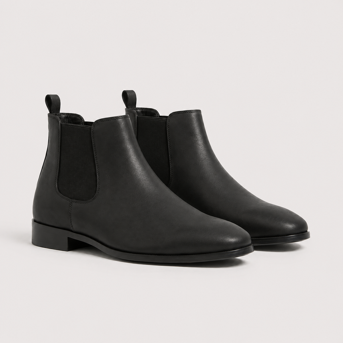 Black leather Chelsea boots with elastic side panels, a round toe, and a low block heel on a light background.