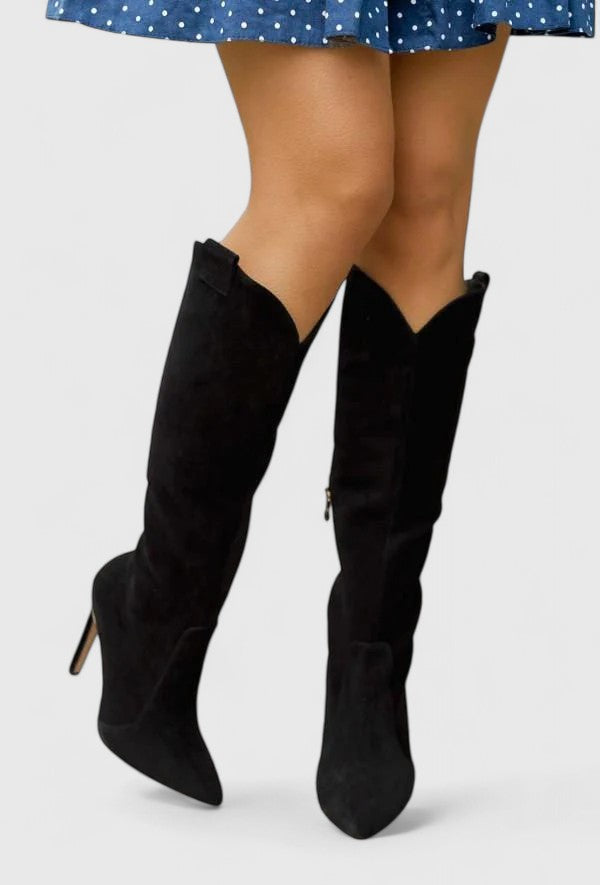 Black suede knee-high heeled boots worn with a blue patterned dress.