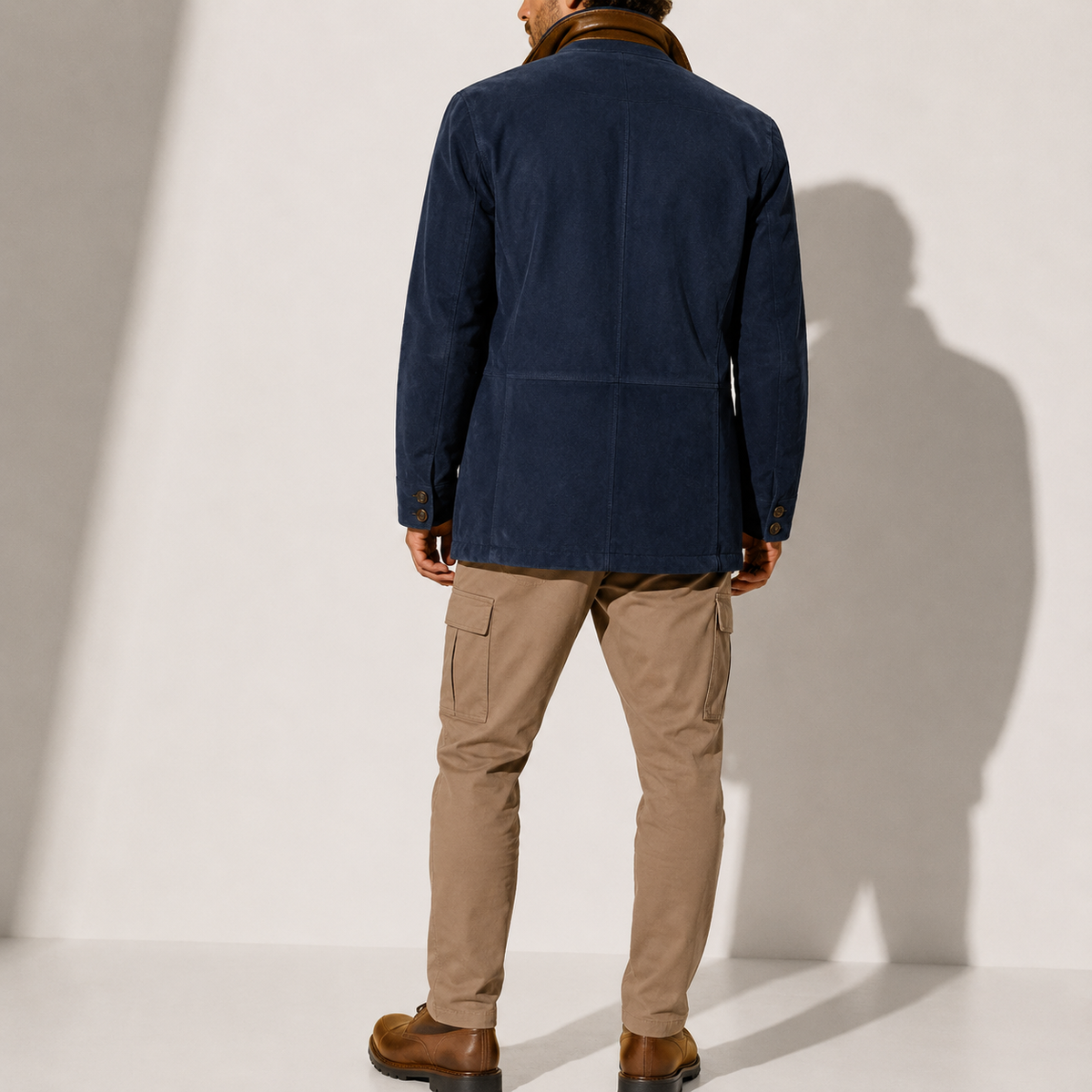 A man wearing a navy blue suede blazer jacket with a stand collar, tailored fit, and button front, back view