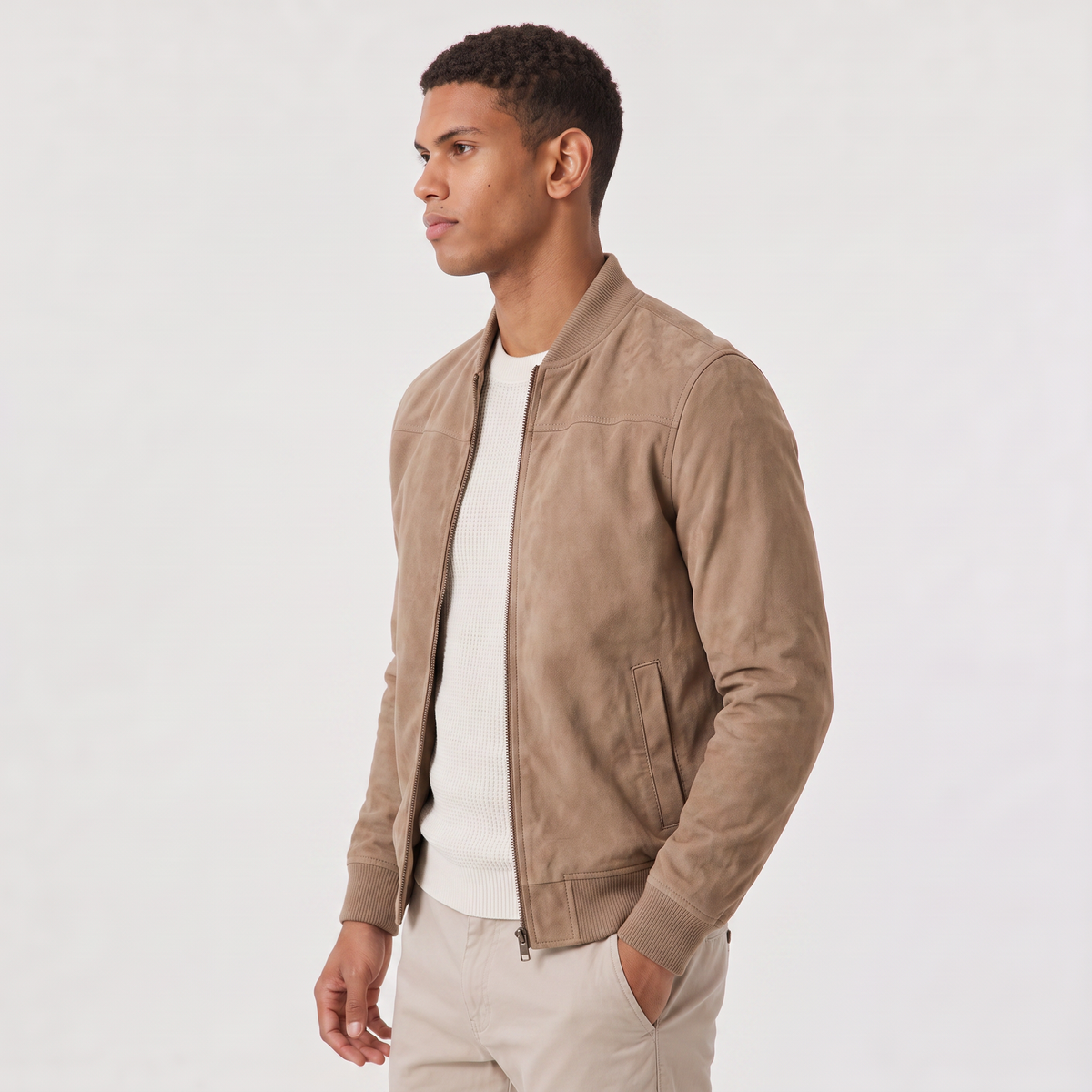 A man wearing a brown suede bomber jacket with a zip-up front and stand collar, seated on a bench