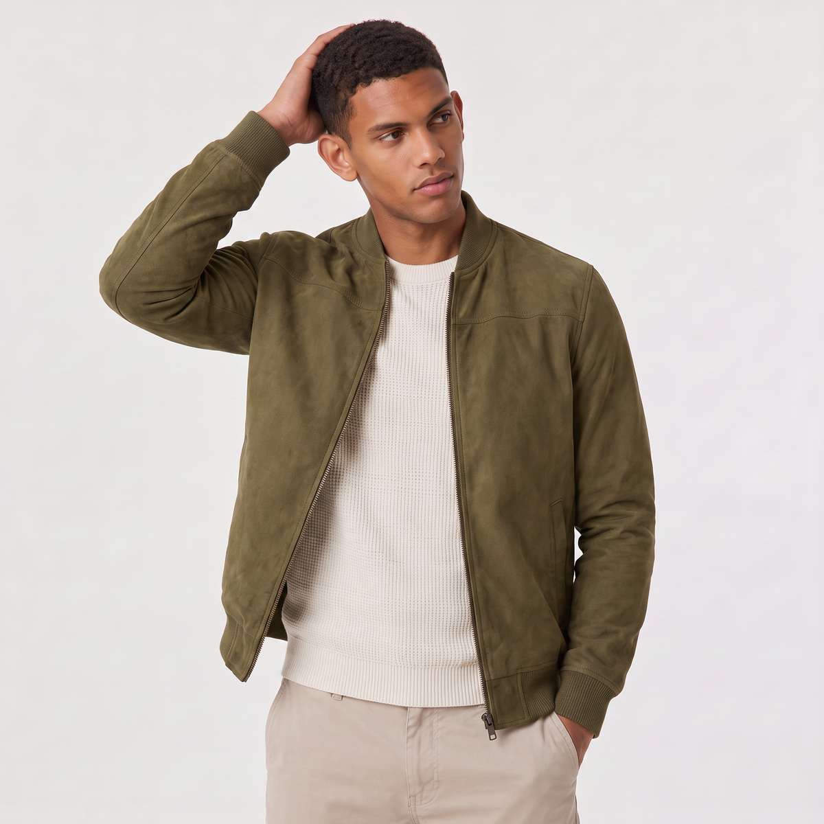 A man wearing an olive green suede bomber jacket with a zip-up front, stand collar, and ribbed cuffs