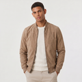 A man wearing a brown suede bomber jacket with a zip-up front, stand collar, and ribbed cuffs