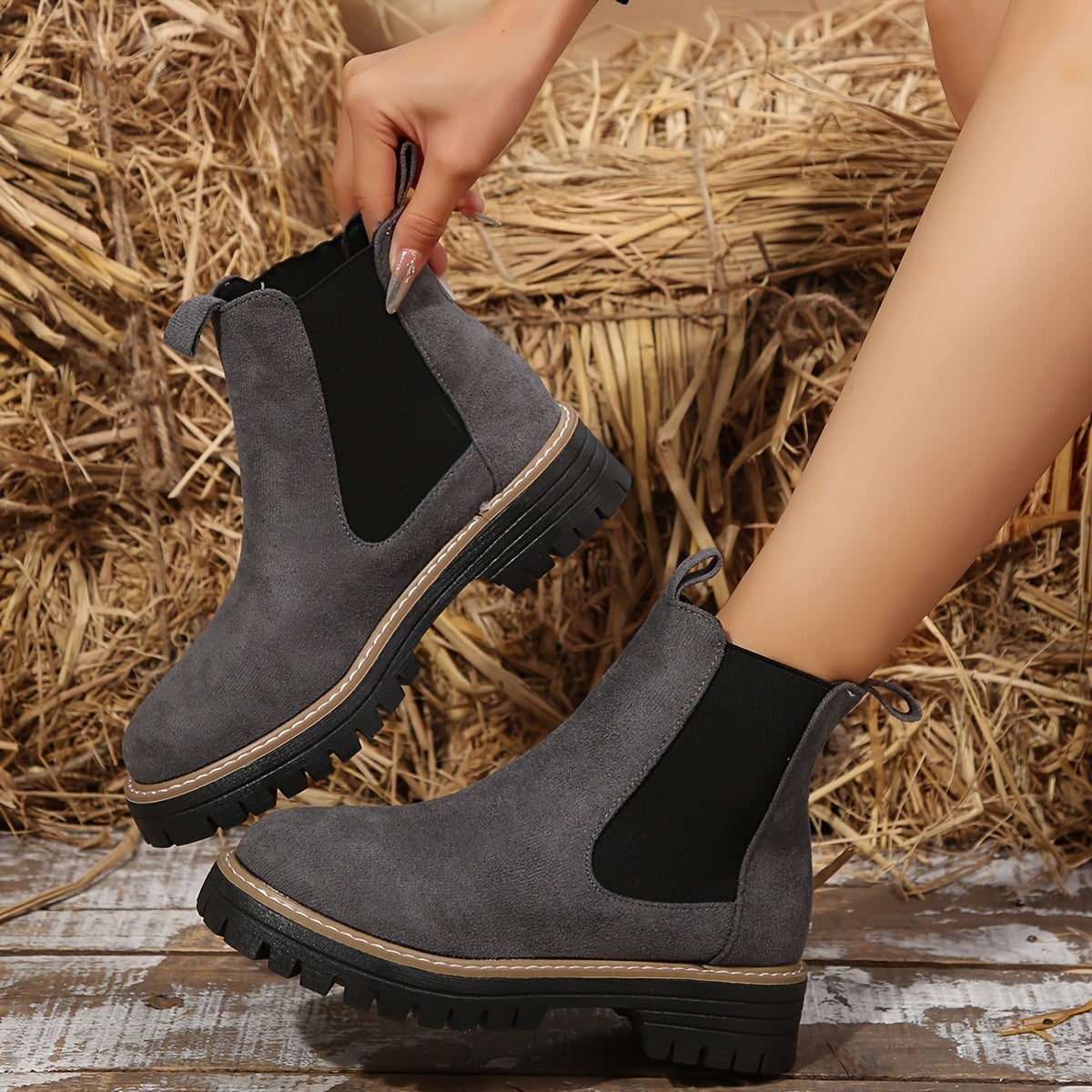 Woman pulling on a gray suede Chelsea ankle boot by the heel tab, showing the elastic gusset