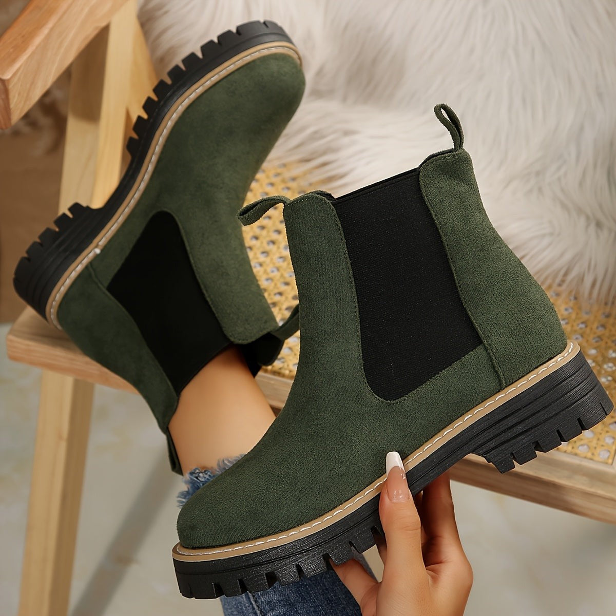 Pair of green suede Chelsea ankle boots for women held up to show the lug sole and stitched welt