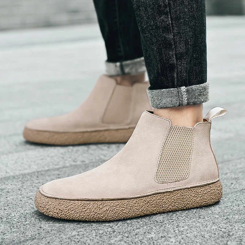 Beige suede Chelsea sneaker boots with knit gore panels and a chunky, textured brown rubber sole worn with jeans.