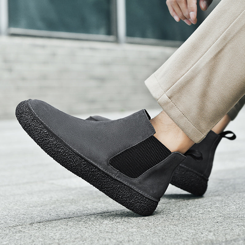 Close-up of black Chelsea boots worn with light-colored trousers, showing the side profile and thick sole.
