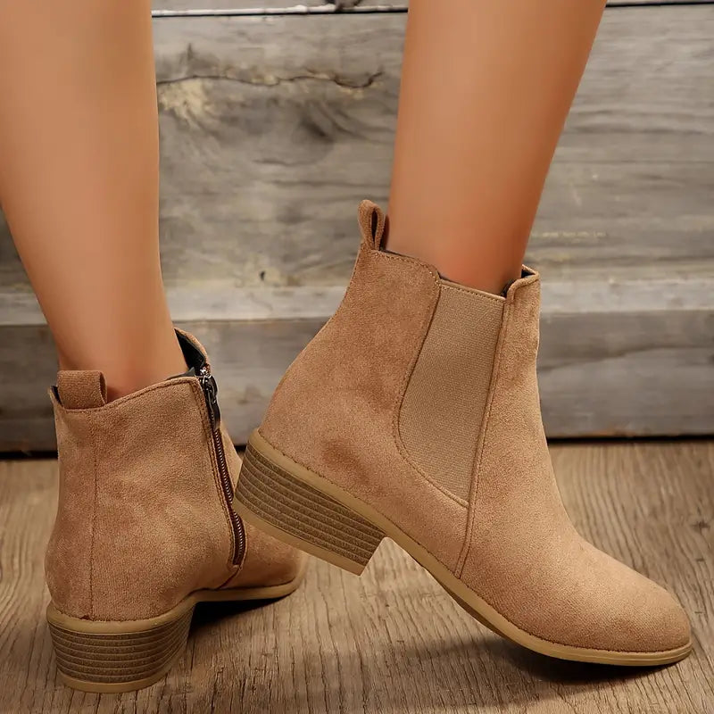 Beige suede pointed-toe Chelsea boots for women with side zip and elastic panel, worn on a wooden deck