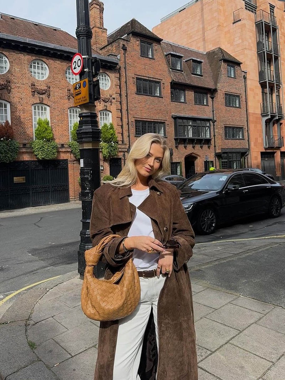 A woman wearing a brown suede trench coat with a belted waist and longline fit on a city street
