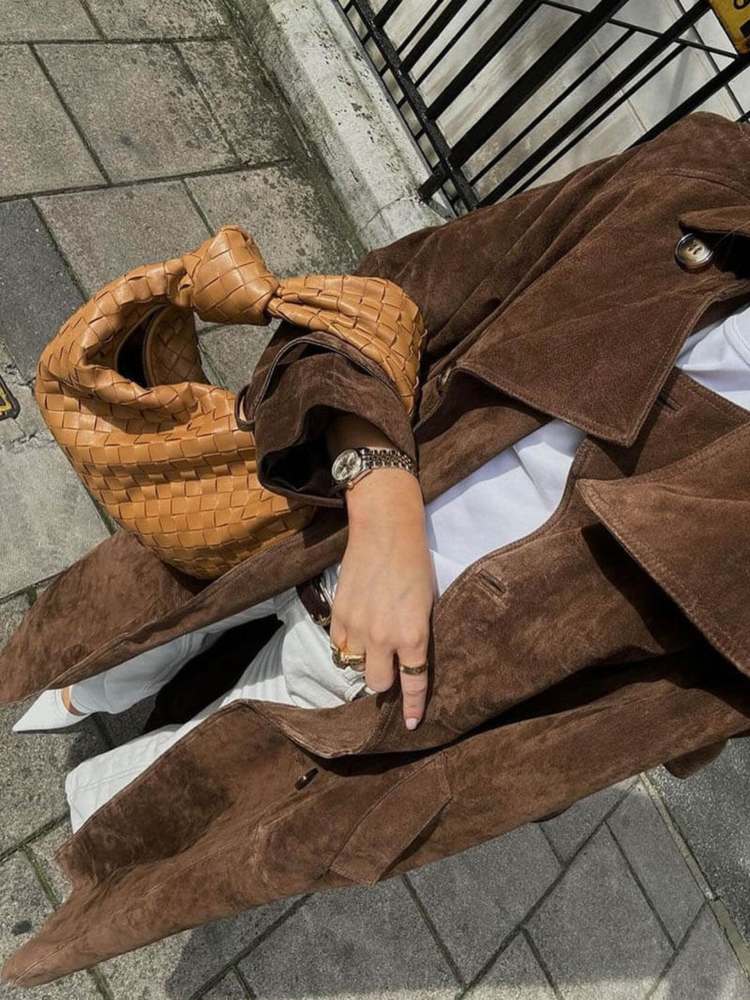 Close-up of a woman wearing a brown suede trench coat, showing the belted waist, double-breasted front, and soft suede texture