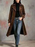 A woman wearing a brown suede trench coat with a longline fit, belted waist, button front, and lapel collar, full-body view