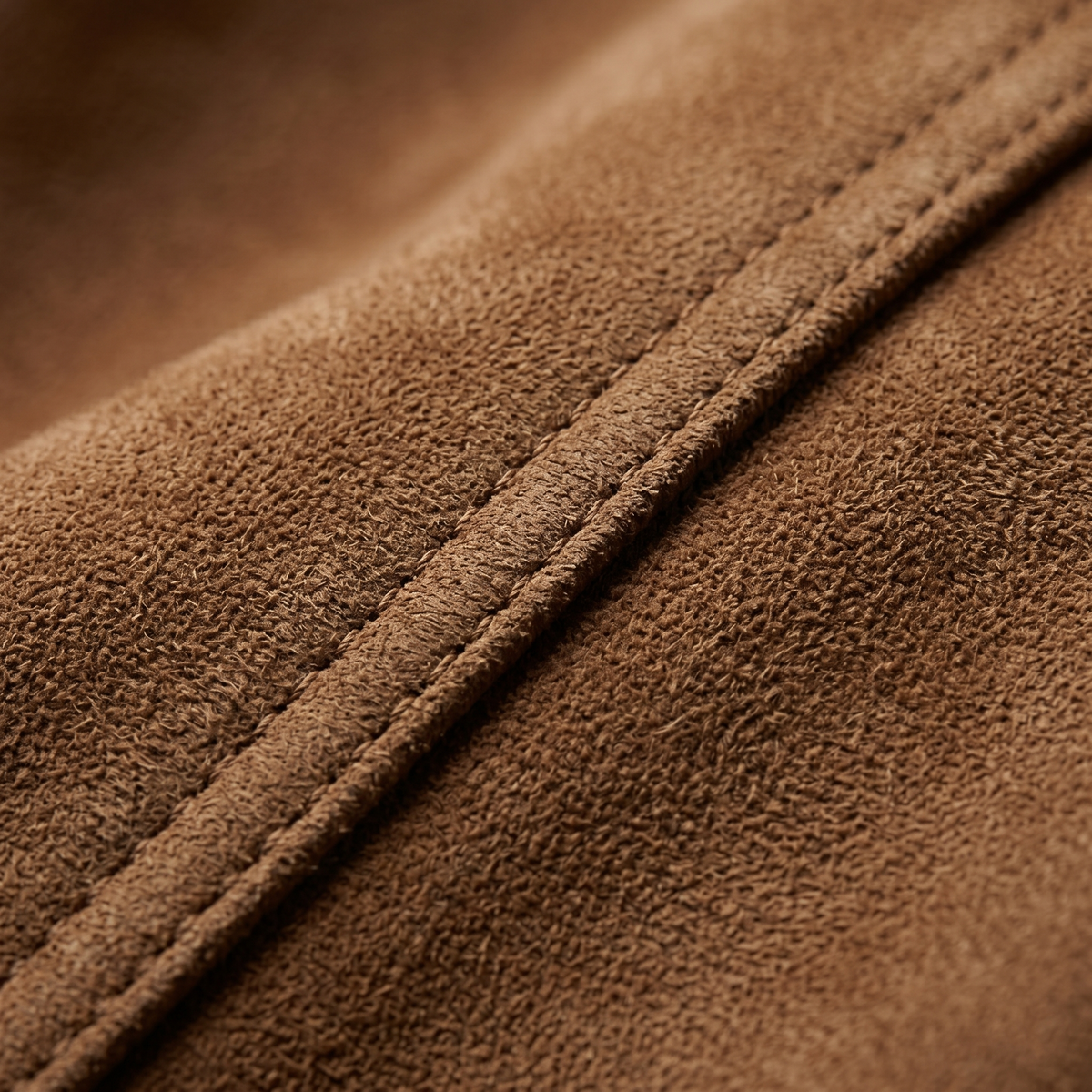 Close-up of brown suede fabric showing its soft textured surface and stitched seam detail