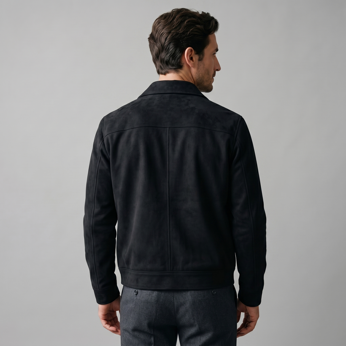 A man wearing a black suede trucker jacket with a button front, stand collar, and chest pockets, back view