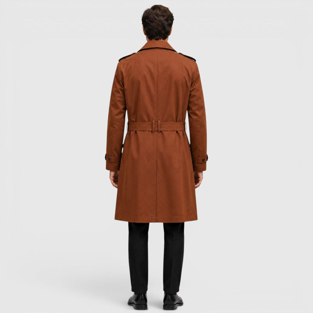 A man wearing a rust brown tailored double-breasted trench coat with an adjustable belt, shown from the back