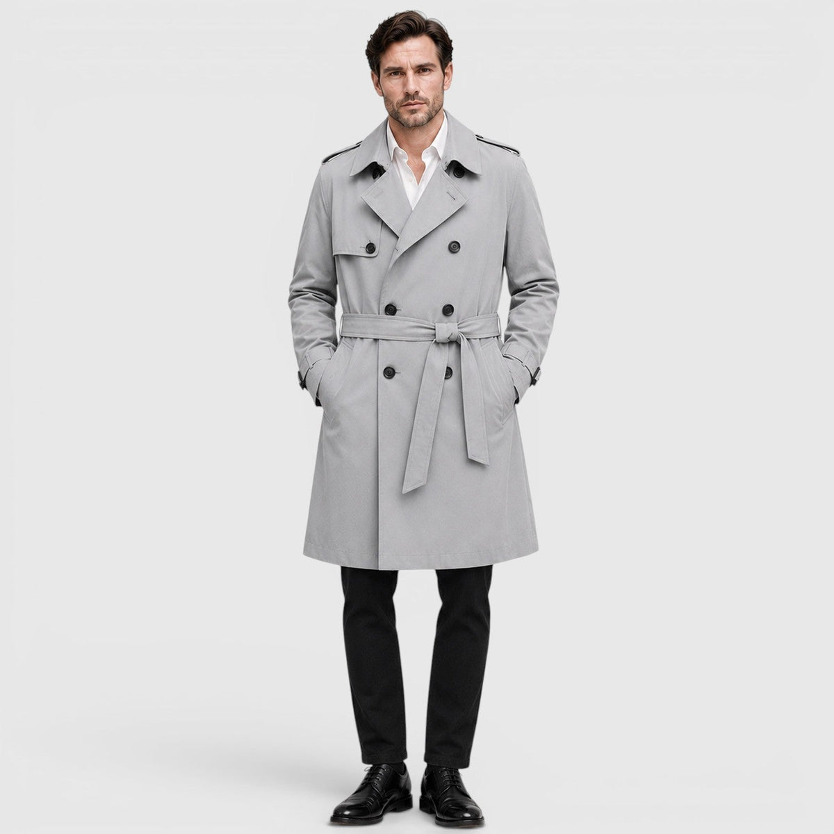 A man wearing a light gray tailored double-breasted trench coat with an adjustable belt and notch lapel