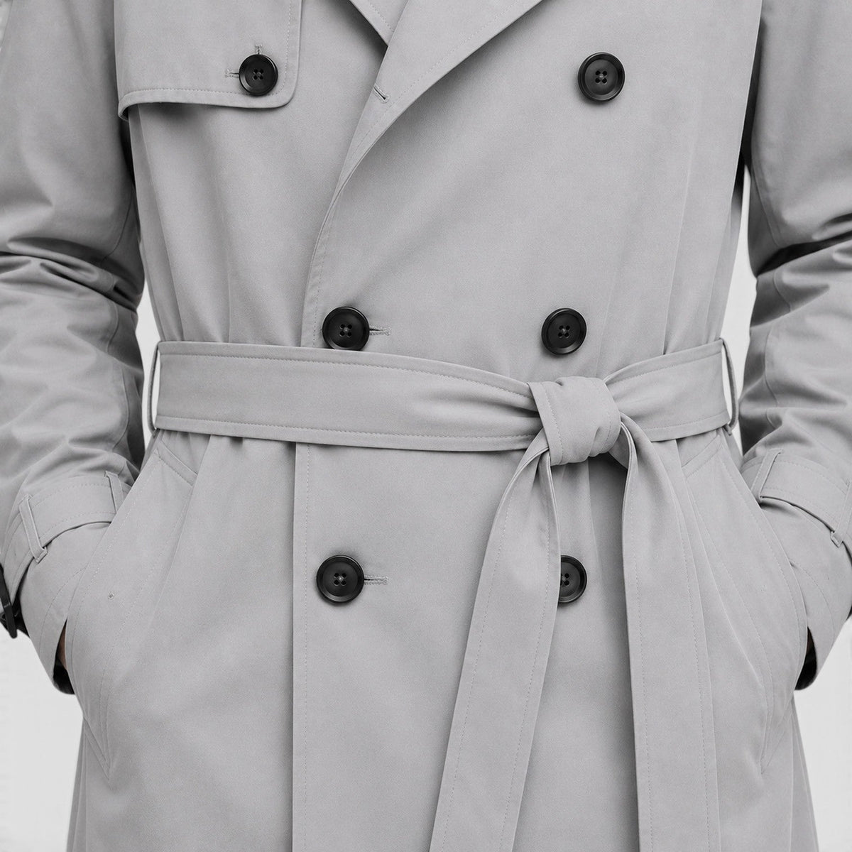 Close-up of a light gray double-breasted trench coat showing the notch lapel, front buttons, and adjustable belt