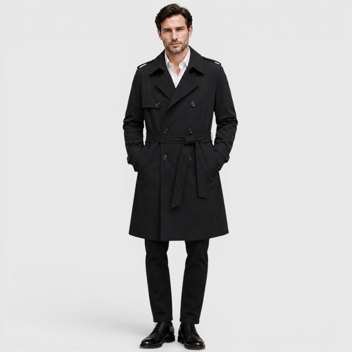 A man wearing a black tailored double-breasted trench coat with an adjustable belt and notch lapel