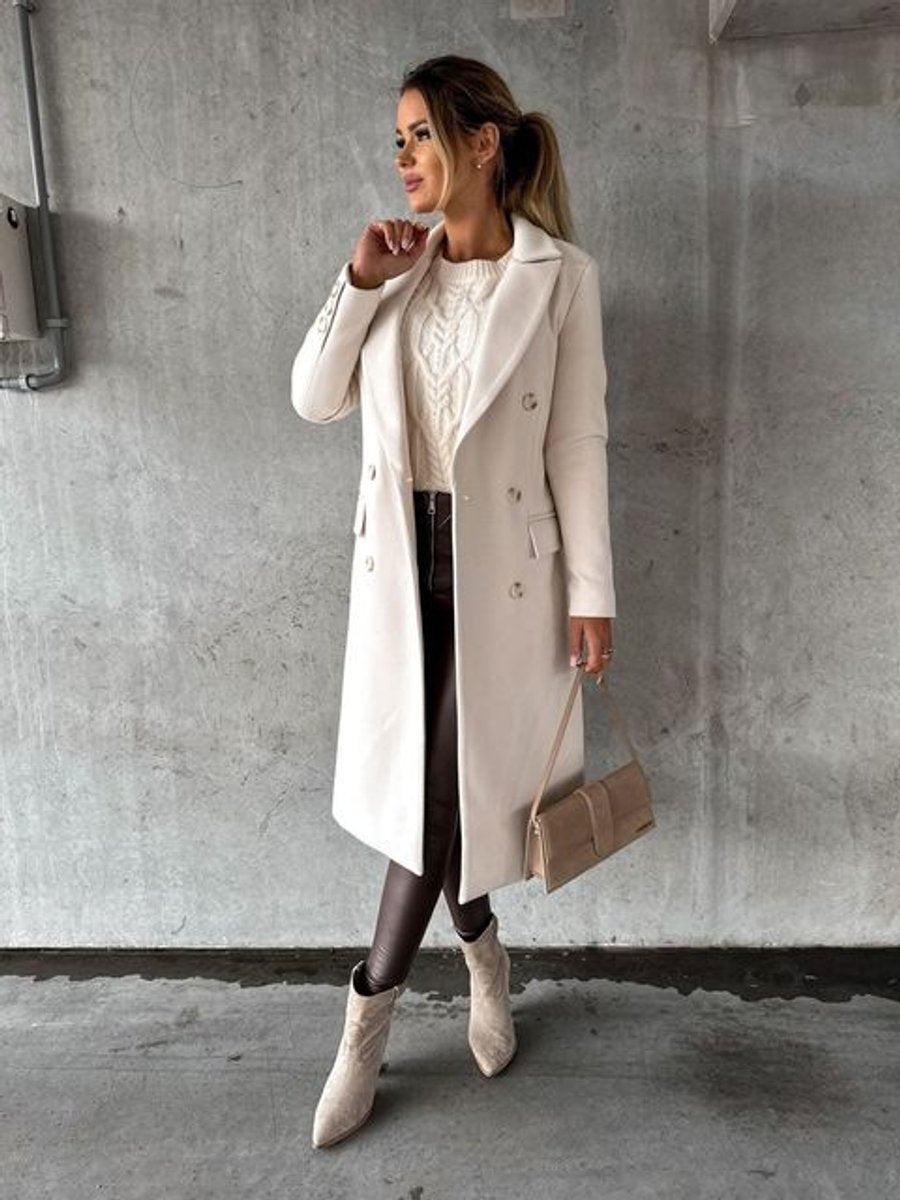 A woman wearing a white wool midi overcoat with a double-breasted front and notched lapels, walking indoors