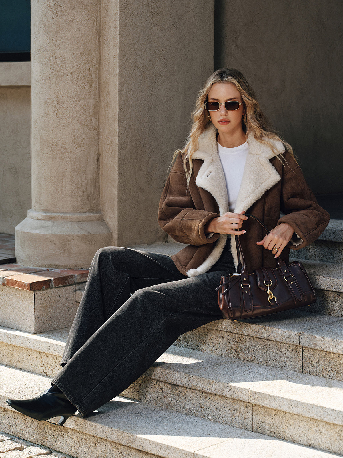 Brown thickened wool shearling jacket worn by a female model seated outdoors, featuring a boxy fit and plush collar