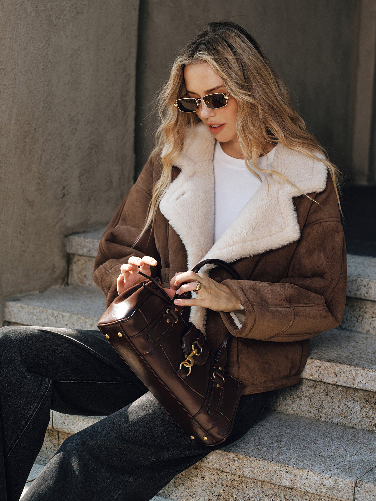 Brown thickened wool shearling jacket worn by a female model seated outdoors, front view with plush lining and welt pockets