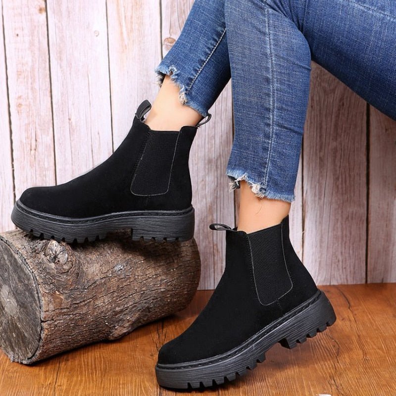 Black platform Chelsea boots for women with elastic side panels, one foot resting on a log