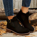Woman pulling on a black vegan suede Chelsea boot with buckle strap, worn with cropped jeans