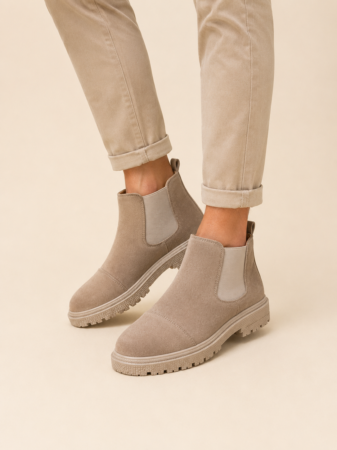 Man pulling on a beige vegan suede Chelsea boot by the rear tab, worn with cuffed black jeans