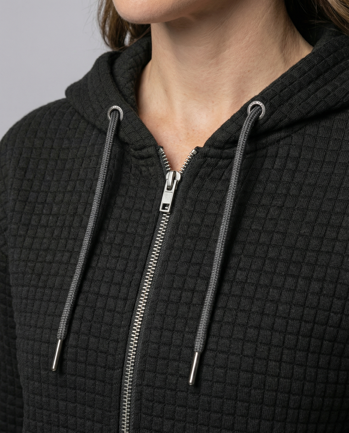 Black fitted waffle knit zip-up hoodie for women close-up showing the textured waffle knit fabric, hood, and zipper