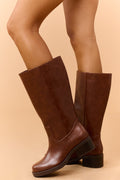 Brown knee-high boots with a low block heel worn with bare legs.