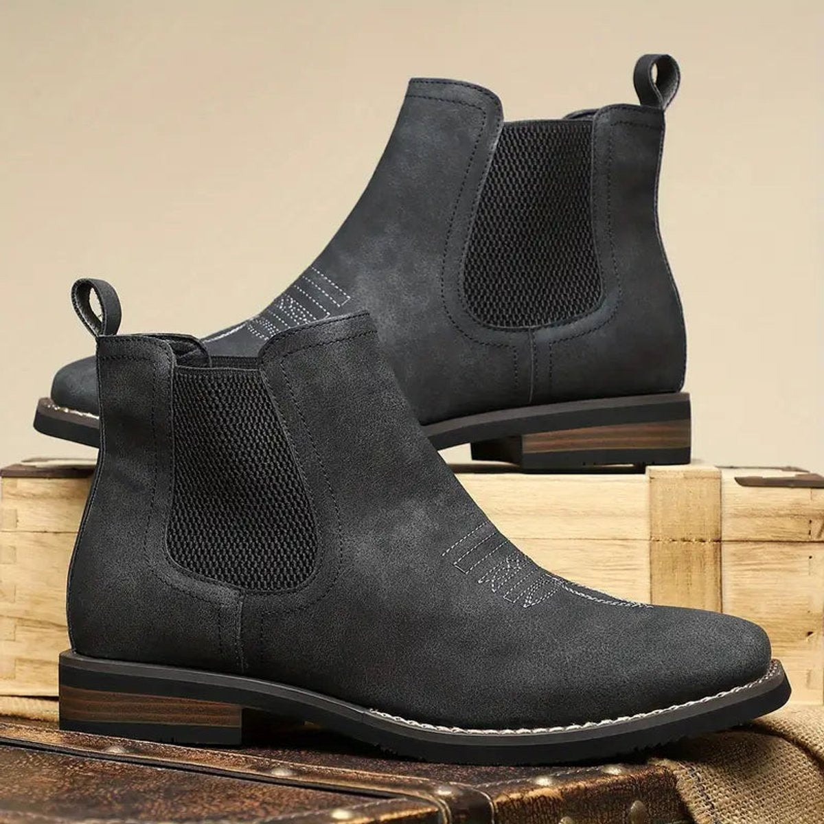Black wide toe box Chelsea boots for men with elastic side panels and stacked heel, on a wooden crate