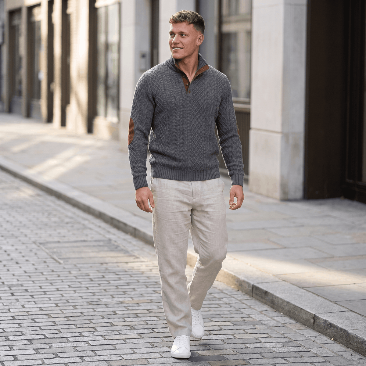 Man wearing a gray cable knit Henley sweater paired with light-colored trousers while walking in an urban setting.