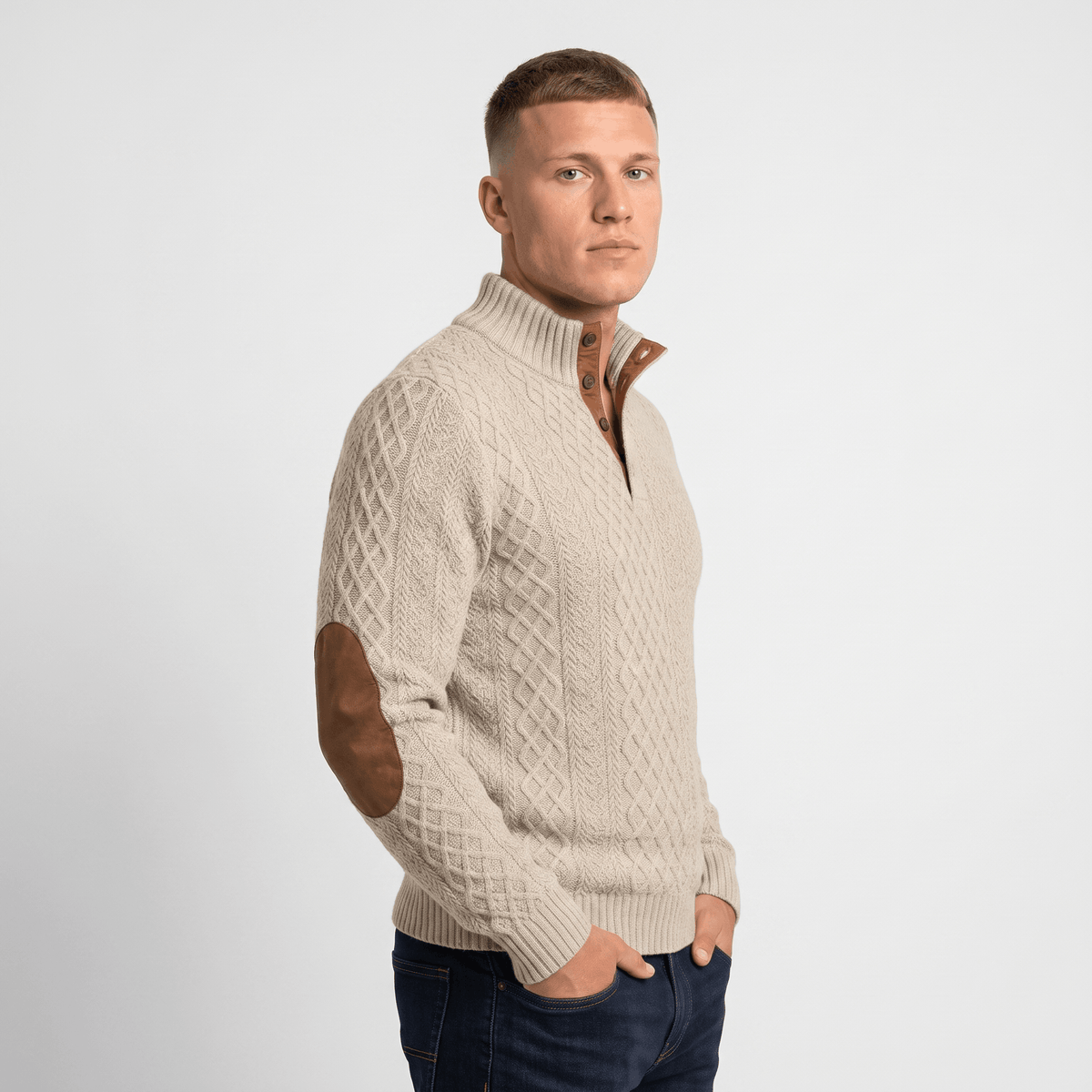 Side view of a man wearing a cream cable knit Henley sweater featuring a stand collar, button placket, and faux suede elbow patches.