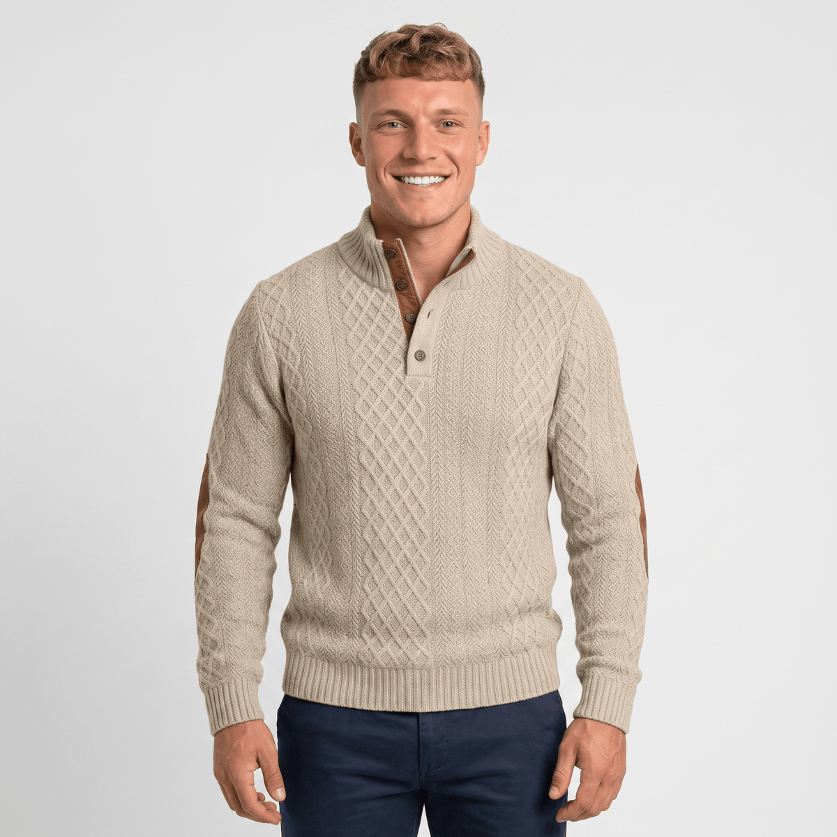 Man wearing a cream cable knit Henley sweater with a stand collar, button placket, faux suede elbow patches, and a classic fit.