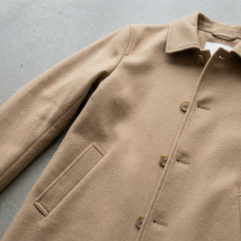 Close-up of a beige wool blend mid-length trench coat showing the collar, button closure, and angled pocket
